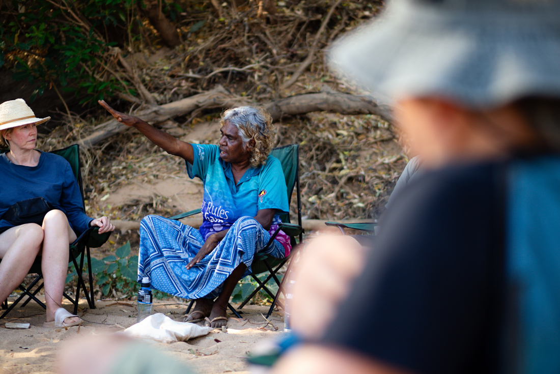 First Nations elder give a talk to seated travellers in the Western Australia outback