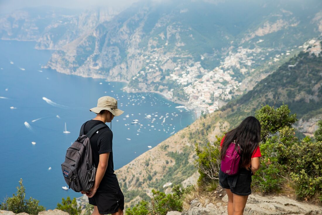 Two travellers hiking on the Path Of The Gods with a great view of the boats and village on Amalfi Coast