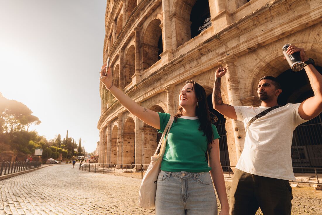 Two smiling travellers take a selfie in front of the Coliseum at dawn, Rome, Italy