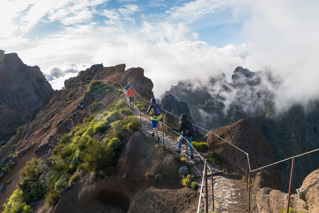 Travellers hike a narrow mountaintop path on the way to Pico do Ruivo in the sunlight of Madeira, Portugal