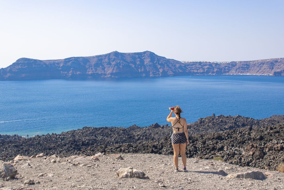Traveller standing near waters edge looking out to a Volcano in Santorini, Greece