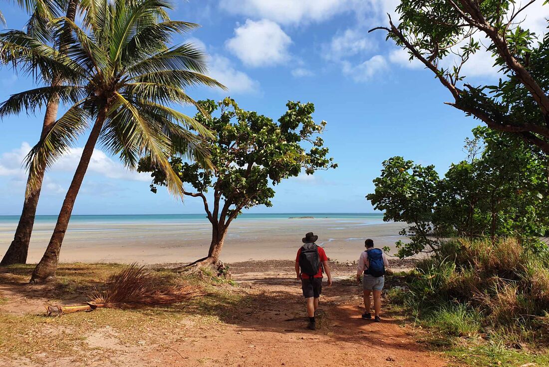 Traveller and leader at the end of a hike to a beach step onto the sand from the last bit of forest in Cape York
