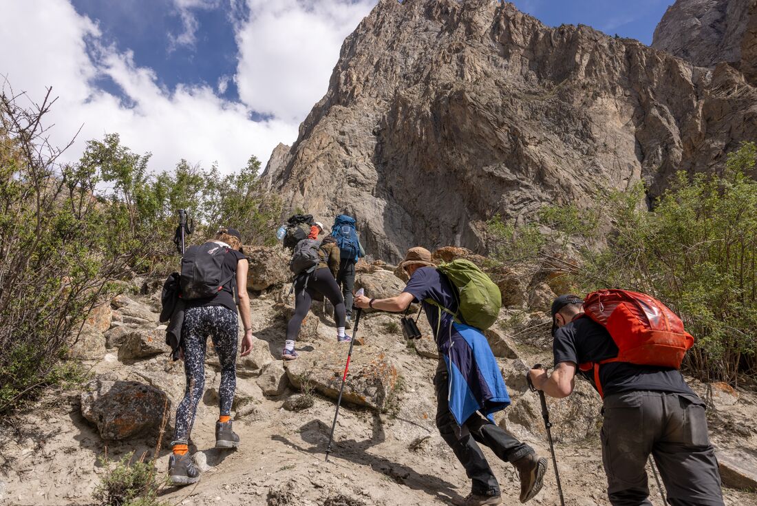 Travellers hiking from Kanday to Mingulo Broq up a sharp incline of rock in Karakoram Mountains