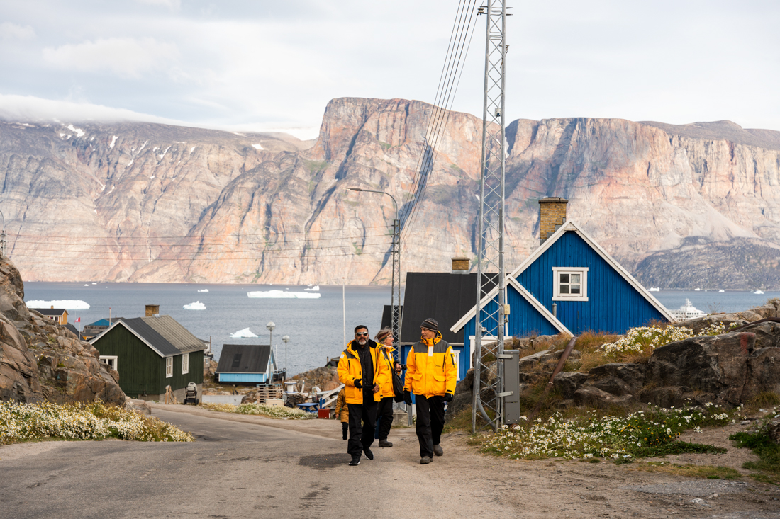 Leader gives a talk to travellers while they walk the streets of Uummannaq with Greenland mountains beyond