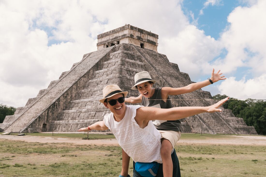 Happy mother and daughter with arms stretched out openly in front of El Castillo, Chichen Itza, Yucatán, Mexico 