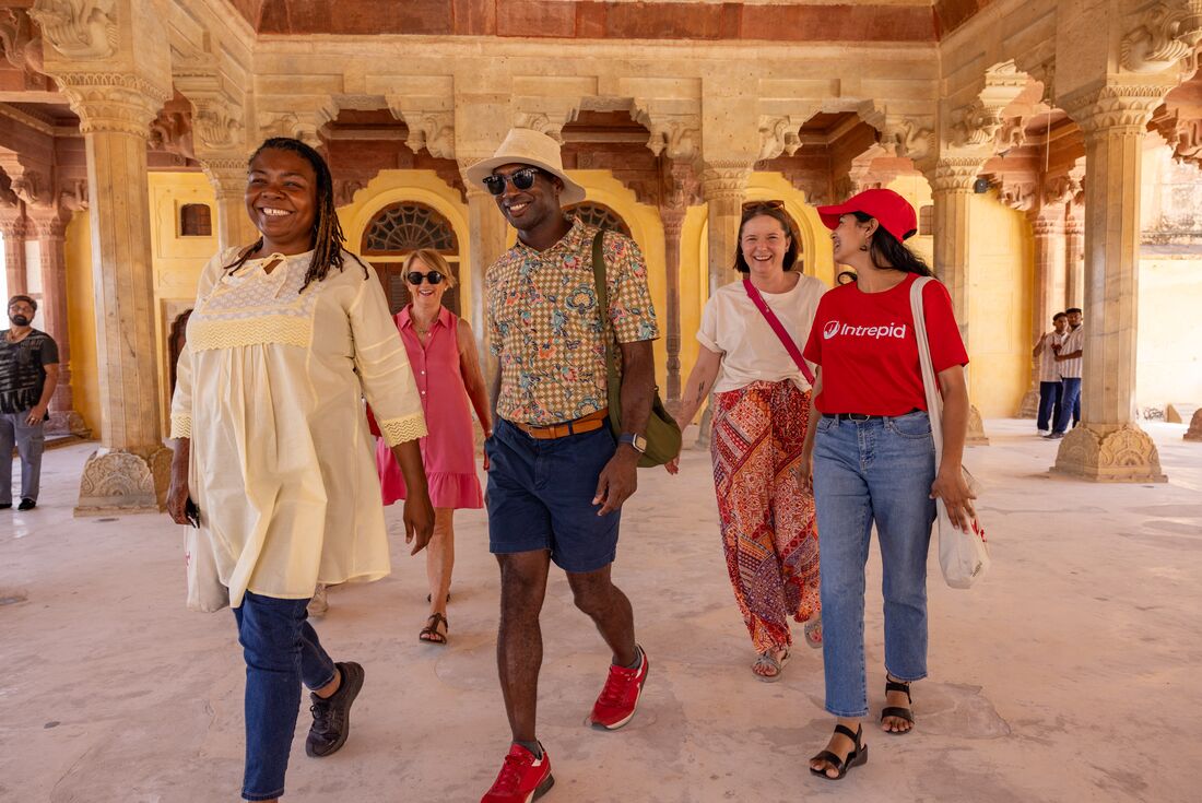 Group of travellers with leader laugh while walking through beautifully carved interior of Amber Fort in Jaipur