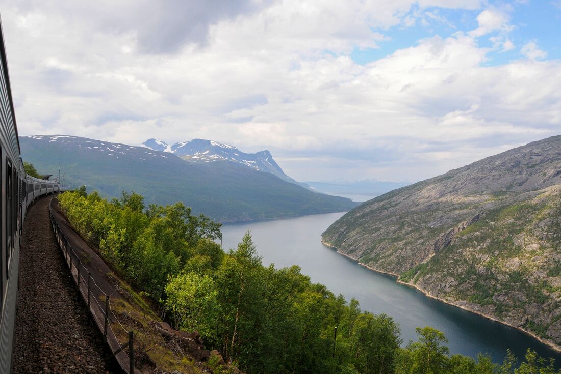 A train rides a high ridge along the Otenfjord with a forest below and mountains looming beyond 