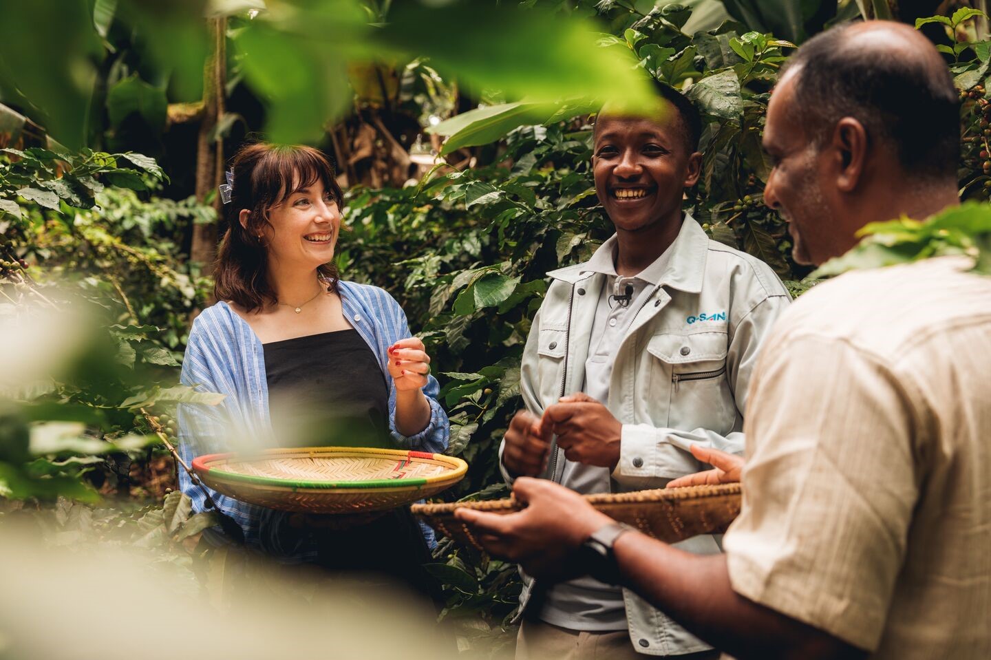 A traveller and two leaders hold baskets containing coffee beans in Tanzania