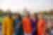 Group of varied ages pose with smiles in colourful elegant clothing standing at a distance in front of the Taj Mahal