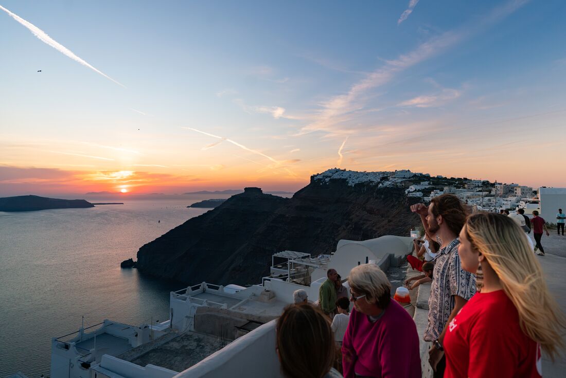 Intrepid travellers and leader look out at sunset over the Aegean Sea from a Santorini balcony