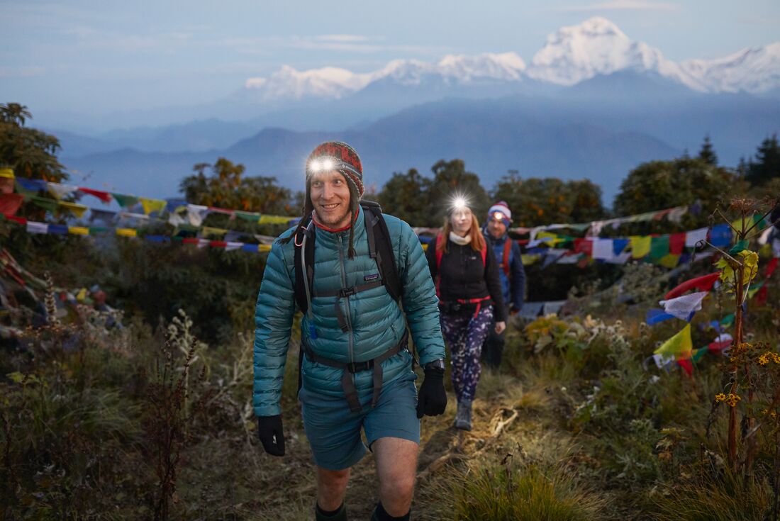 Travellers wearing headlamps and backpacks hike toward a hilltop for a spectacular sunset view in Nepal