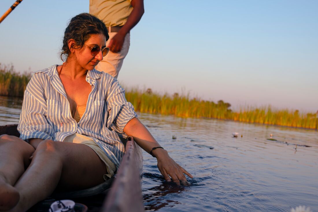 Traveller running fingers along water on Okavango Delta while riding in canoe, Botswana