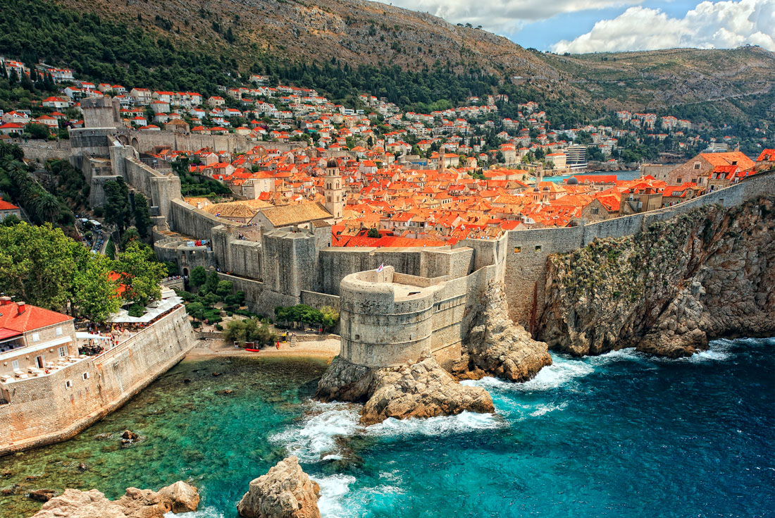 The stone fortification walls of Dubrovnik and the orange rooves beyond seen from a cliff across the sea in Croatia