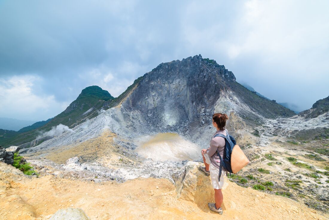 Traveller looks out at caldera emitting heat and steam at top of Mt Sibayak in Sumatra from end of a hike
