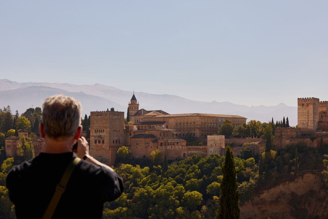 Alhambra Fortress with mountains in the background and traveller taking a photo of the view in the foreground, Granada, Spain