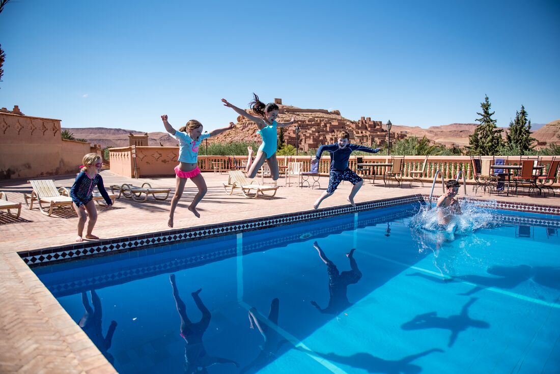 Group of Intrepid traveller children jumping into a pool with the kasbah of Ait Benhaddou in the background