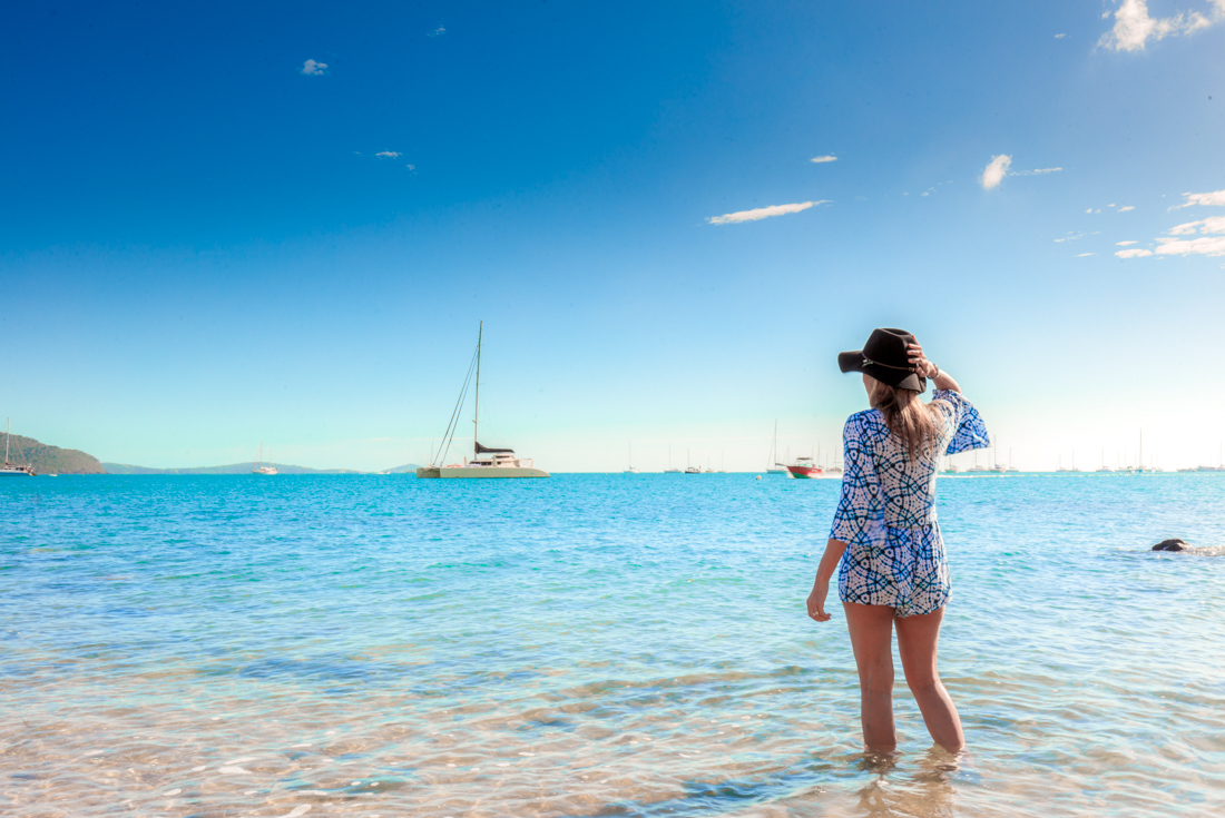 18 to 35s travellers looks out over Whitsunday Island beach with boats anchored off shore