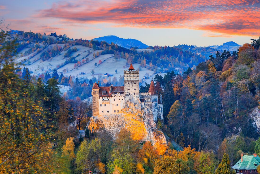 Wide view of medieval Bran Castle during sunset with warm autumn colours of surrounding trees, Transylvania, Romania