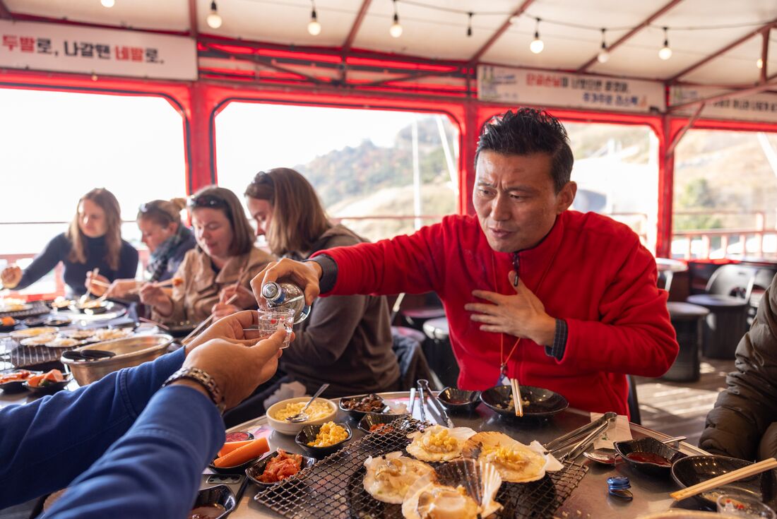 Leader pours a traveller a drink while enjoying a seafood barbque lunch in Busan