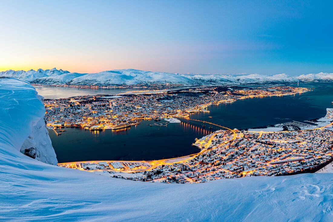 High vantage look out over city of Tromso in winter glowing building lights with blanket of snow on the coast