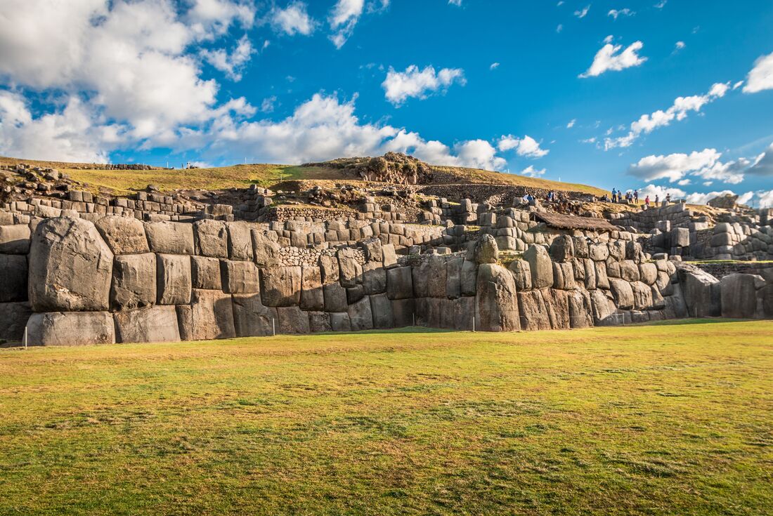 Towering stone walls of Sacsayhuaman archaeological site with travellers atop them in the distance