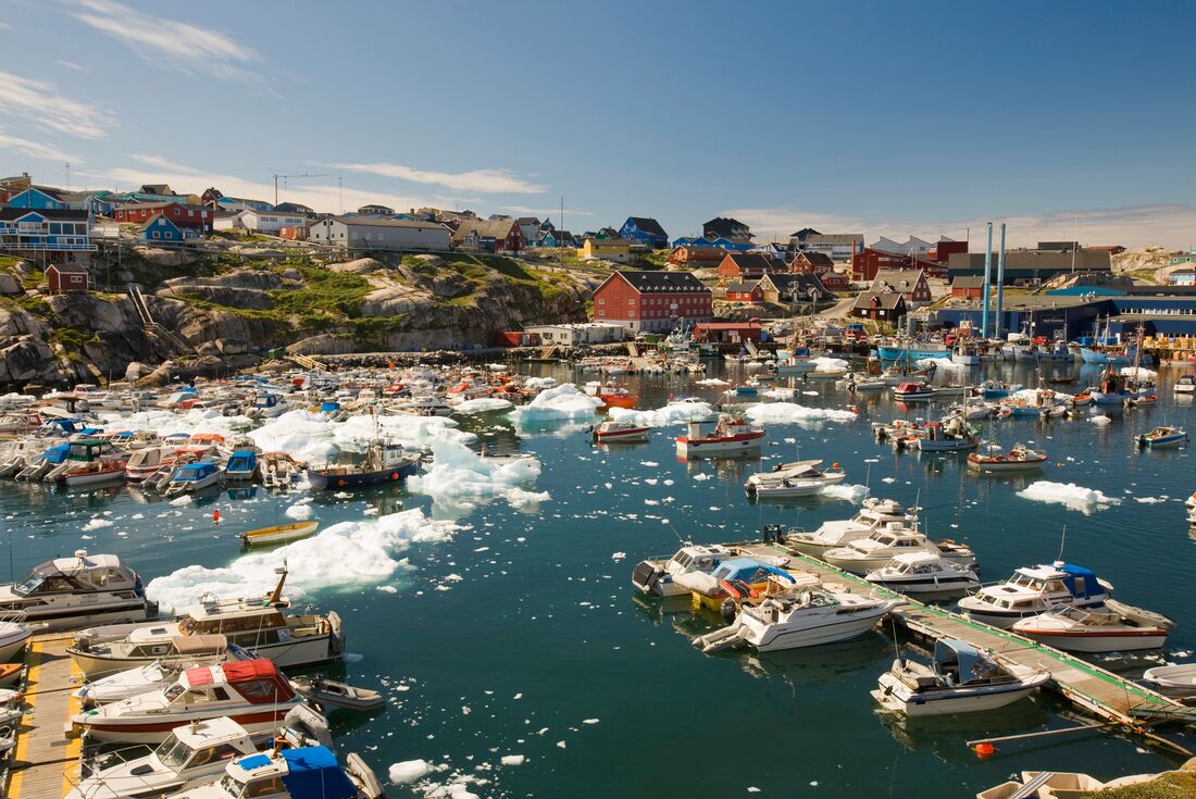 Ilulissat harbor with a number of docked boats and small icebergs in the harbor, buildings and town beyond