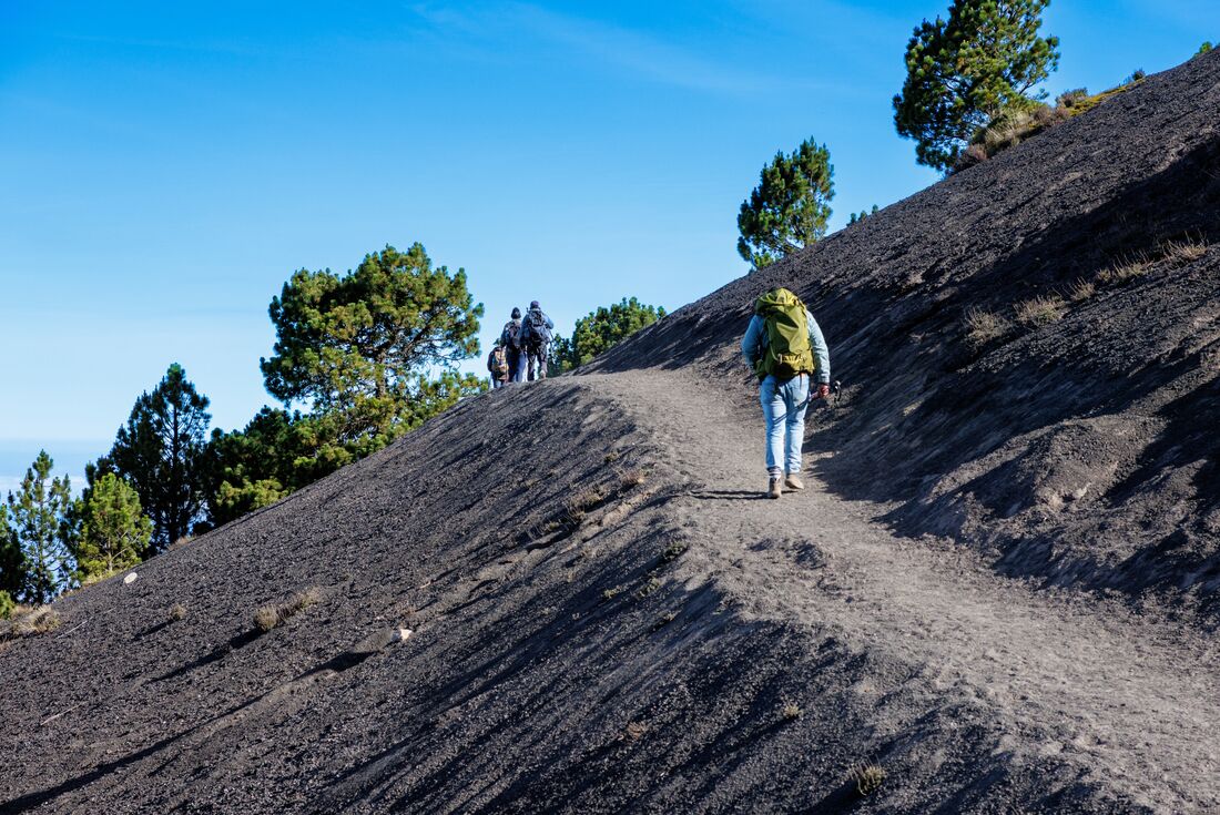 Intrepid travellers on a volcanic rock ridge with backpacks hike up the slopes of Acatenango in Guatemala 